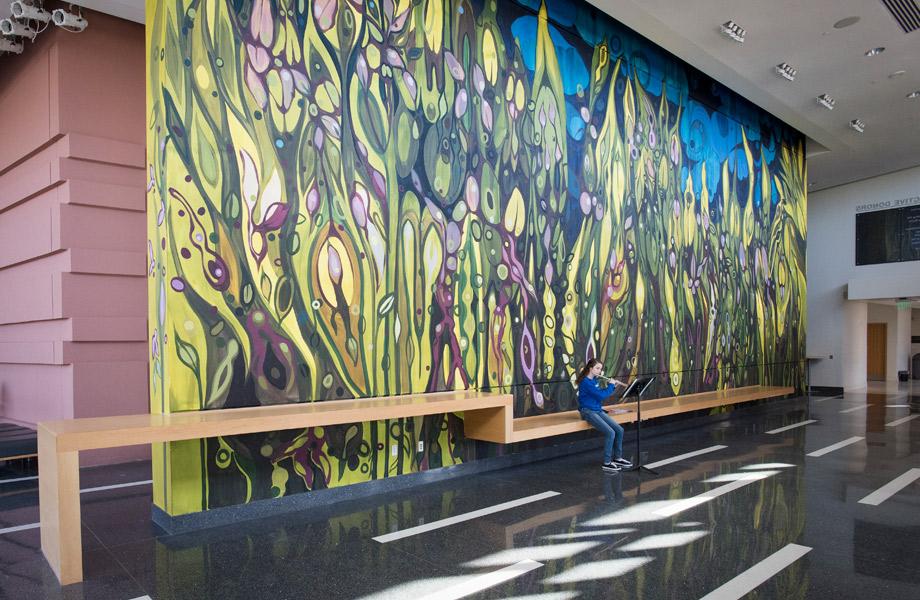 A student playing an instrument in the lobby of Music building, in front of mural